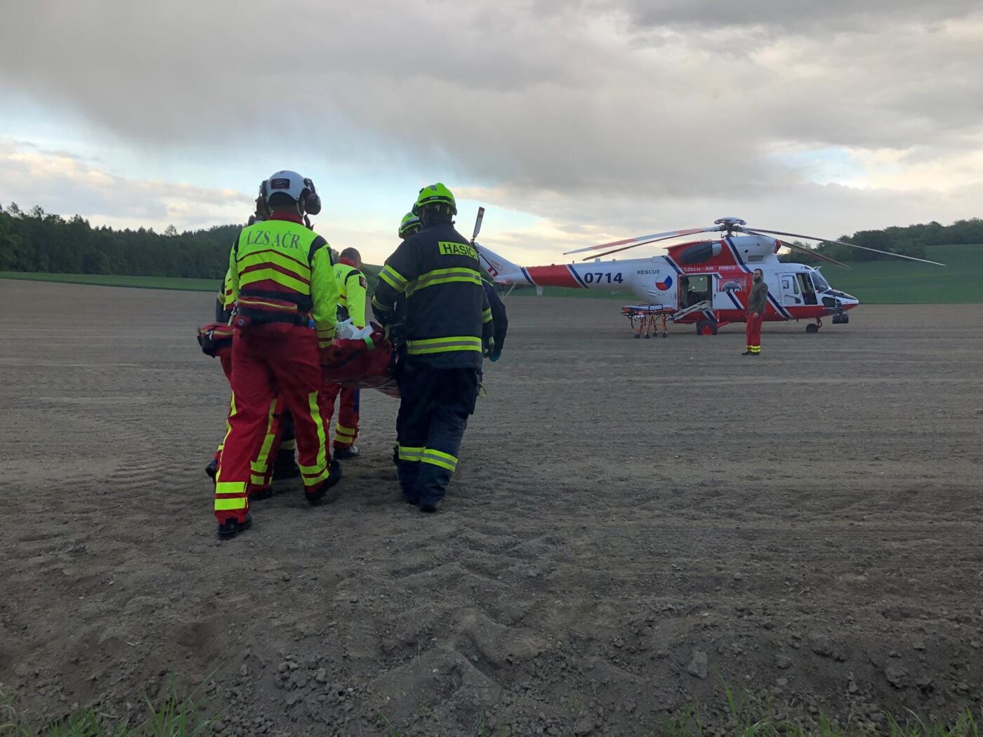Zraněného řidiče museli hasiči přenést po poli k vrtulníku. Foto: HZS